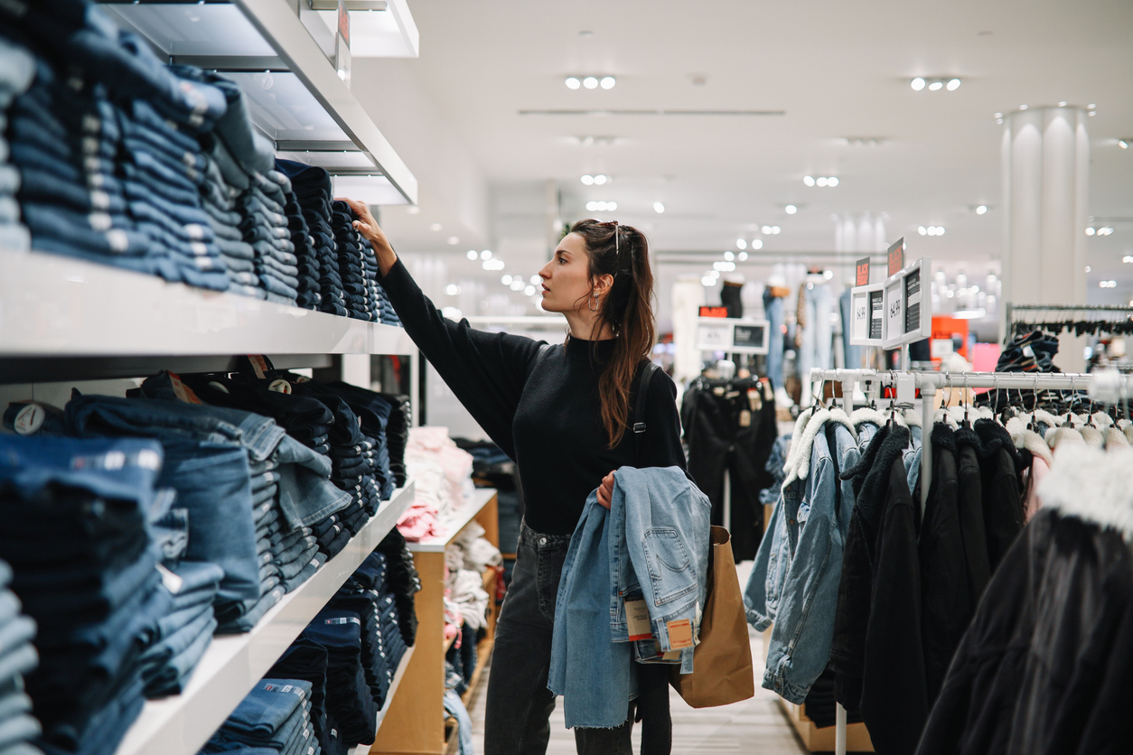 Woman in mid 30s goes shopping for denim jeans in a mall or a clothing store.